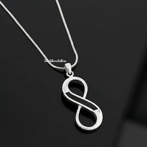 Könnte beinhalten: Eine silberfarbene Halskette mit einem Anhänger in Form eines Unendlichkeitszeichens. Der Anhänger hat eine polierte Oberfläche mit schwarzem Inlay. Die Kette ist eine filigrane Boxkette. Die Worte "The Silver Sellers" sind auf der Kette aufgedruckt.