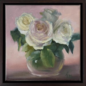 Puede incluir: Pintura al óleo de rosas blancas en un jarrón de cristal transparente, sobre un fondo rosa suave. La obra está enmarcada en un marco de madera marrón oscuro. Las rosas tienen un tono blanco cremoso con hojas verdes.