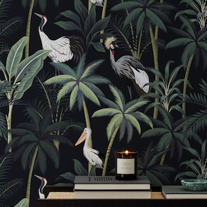 Puede incluir: Papel pintado oscuro con una escena de jungla tropical con palmeras y varias aves, incluyendo grullas y pelícanos. Una vela encendida se encuentra sobre una superficie marrón oscuro con libros y un pequeño cuenco verde.