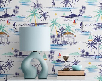 Pode incluir: Um abajur de cerâmica azul com um design curvo único está sobre uma mesa branca com uma pilha de livros e uma tigela azul. O fundo é um papel de parede branco com um tema de ilha tropical com palmeiras, veleiros e água azul.
