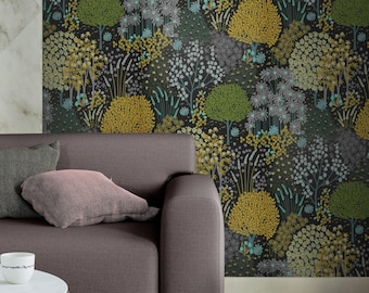Puede incluir: Un sofá gris oscuro con dos almohadas, una verde oscuro y otra rosa claro, se encuentra frente a una pared cubierta con un papel tapiz floral negro y verde. El papel tapiz presenta un patrón repetitivo de árboles y flores estilizados en tonos de verde, amarillo y azul.