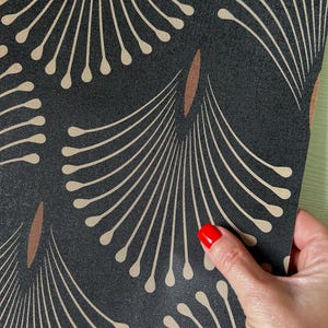 May include: Close-up of a black fabric with a repeating pattern of beige fan-like shapes and brown elongated ovals. The fabric is being held by a hand with red nail polish.