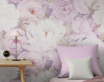 May include: A bedroom scene featuring a floral wallpaper with large, white and pink peony blooms. A wooden table holds a pink lamp and a small black clock. A bed with pink pillows and a striped pillow is in the foreground.