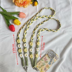 May include: Braided phone straps in green, yellow, and white, adorned with daisy-shaped embellishments. The straps are approximately 110cm and 95cm long. A phone case with a butterfly design is also visible.