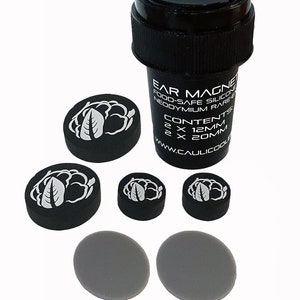 May include: A set of black and grey ear magnets with a white leaf design. The magnets come in two sizes, 12mm and 20mm. The set includes a small black container with the text "Ear Magnets, Food-Safe Silicone, Neodymium Rare Earth, Contents: 2 x 12mm, 2 x 20mm, www.caullicoole.com".