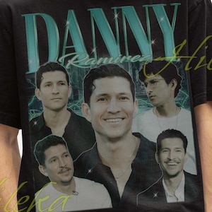 May include: Black t-shirt featuring the name "DANNY" in teal block letters above a collage of images of a man. The shirt also has the text "Ramirez" and "Hileka" in a cursive font. The person in the image is wearing a black bucket hat.