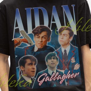 May include: Black t-shirt featuring a collage of images and the name "AIDAN" in large, bold letters. The images appear to be of a person, with the name "Gallagher" below. The person is wearing a black bucket hat.