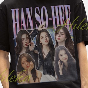Könnte beinhalten: Schwarzes T-Shirt mit einer Grafik von Han So-hee und dem Text "HAN SO-HEE" in einer lila, Vintage-artigen Schrift. Das T-Shirt hat einen Rundhalsausschnitt und kurze Ärmel. Das Bild enthält einen schwarzen Fischerhut.