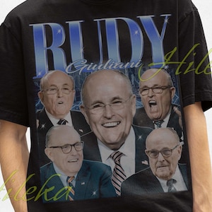 Könnte beinhalten: Schwarzes T-Shirt mit einem Grafikdesign mit dem Namen "RUDY" in Blau, zusammen mit mehreren Bildern eines Mannes. Die Person trägt einen schwarzen Fischerhut.