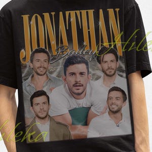 Puede incluir: Camiseta negra con diseño vintage y letras doradas "JONATHAN BAILEY". Presenta un collage de imágenes de Jonathan Bailey. La persona lleva un sombrero de pescador negro.