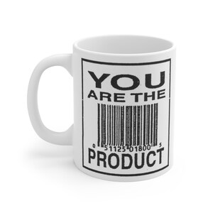 May include: A white ceramic mug featuring a black rectangular graphic with the text YOU ARE THE PRODUCT printed in bold capital letters above and below a central barcode design. The mug has a curved handle on the left side and a smooth finish.