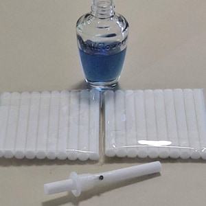 Puede incluir: Un juego de varillas difusoras blancas, una botella de vidrio transparente con un líquido azul y una varilla difusora de plástico blanca.