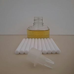 May include: A clear glass bottle with yellow liquid, white diffuser sticks, and a plastic diffuser cap. The bottle has the text "Yankee Candle" on it. The diffuser sticks are arranged in a row, and the cap is in the foreground.