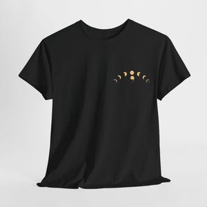 Puede incluir: Camiseta negra con un gráfico de fases lunares doradas y un punto y coma.