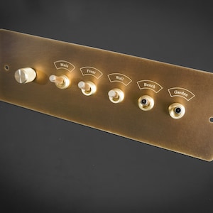 May include: A brass wall plate with six switches and a knob. The switches are labeled "Main", "Front", "Wall", "Bench", and "Garden".
