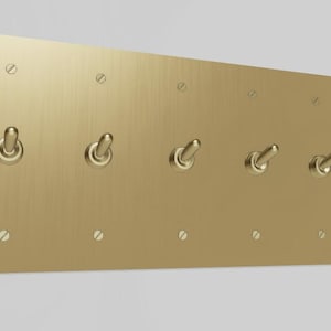 May include: A brushed gold metal light switch plate with five toggle switches.
