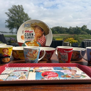 Może przedstawiać: Kolekcja zabytkowych naczyń z motywem Kellogg's Corn Flakes i Rice Krispies. Zawiera kubki, miski, duży talerz i tacę do serwowania z czerwoną obwódką w kropki. Elementy zawierają kolorowe ilustracje maskotek i marki płatków.
