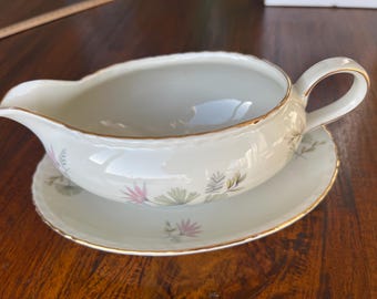 May include: A white porcelain gravy boat with a floral design and gold trim. The boat is sitting on a matching saucer.