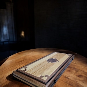 Puede incluir: Un tablero de juego de madera con un diseño de incrustaciones de nogal. El tablero está cerrado y tiene un acabado marrón oscuro.