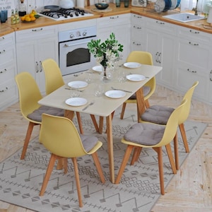 May include: A white kitchen table with a light wood top and four yellow chairs. The table is set with plates, silverware, and glasses. There is a vase of flowers in the center of the table.