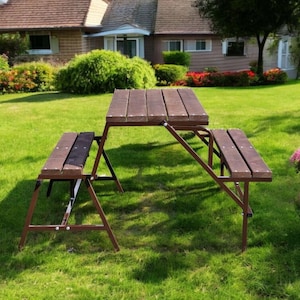 Op de afbeelding: Een bruine houten picknicktafel met aangehechte banken, op een groen gazon. De tafel en banken hebben een lattenontwerp en worden ondersteund door bruine metalen frames. De scène speelt zich buiten af, met een huis en landschapsarchitectuur op de achtergrond.