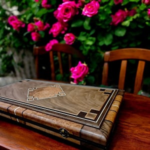 May include: A wooden game board with a walnut veneer and intricate inlaid designs. The board has a diamond-shaped centre piece and a dark brown border. The board is sitting on a wooden table.