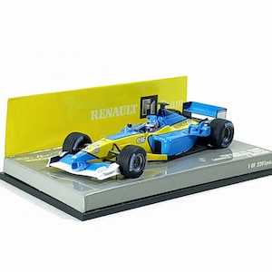 May include: A blue and yellow Renault F1 race car model on a display stand. The model has black tires and the text "RENAULT F1" is visible on a yellow background. The model is 1 of 2201 pieces.