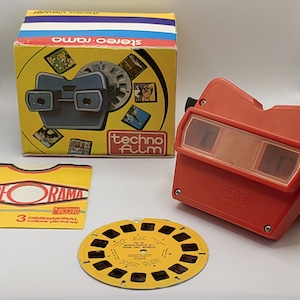 Peut inclure: Un visionneuse 3D en plastique rouge avec une bobine de photos 3D jaune et noire. Le visionneuse a une fenêtre en plastique transparent pour visualiser les photos 3D. La bobine est étiquetée "Panorama de la Mano del Mundo" et fait partie d'un ensemble "Technofilm".