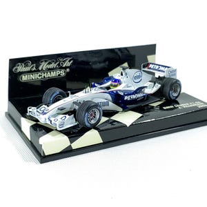 May include: A detailed model of a BMW Sauber F1 car, predominantly white and blue, with sponsor logos. The model sits on a black base with a checkered pattern and a display stand. The text "MINICHAMPS" is visible.