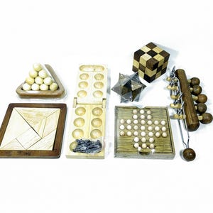 Può includere: Una collezione di rompicapo in legno, tra cui un tangram, un cubo, un puzzle a forma di stella, un gioco di pioli, un triangolo con palline, una tavola di Mancala e un puzzle con palla e catena. I puzzle sono in varie tonalità di marrone e beige.