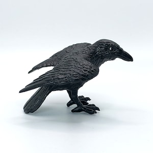 May include: A black raven figurine with detailed feathers and a realistic pose. The raven is perched on a white surface.