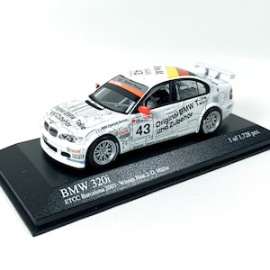May include: A white BMW 320i race car with the text "Original BMW Teile und Zubehör" and the number "43" on the side. The car is on a black display base with the text "BMW 320i ETCC Barcelona 2003 Winner Heat 2. D. Müller 1 of 1,728 pcs."