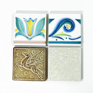 Può includere: Quattro piastrelle quadrate in ceramica con disegni decorativi. Una piastrella presenta un motivo floreale giallo e blu, un'altra ha un motivo a onde blu e verdi, una terza raffigura un Pegaso marrone e l'ultima ha un motivo maculato.