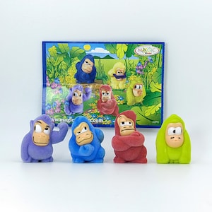 Puede incluir: Colección de figuras de gorilas flocados de colores con diversas expresiones. Las figuras son en tonos morado, azul, rojo y verde, con caras color canela. Una tarjeta de fondo azul con gorilas de dibujos animados está detrás de las figuras.