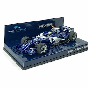 May include: A blue and silver Williams F1 race car model on a display stand. The model has sponsor logos and the text "WILLIAMS FW28 2006 - M. Webber". The display stand has the Williams F1 Team logo.