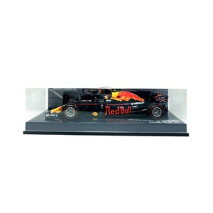 以下が含まれることがあります： ディスプレイケースに入った、レッドブルF1レーシングカーの模型。車体は黒を基調とし、赤と黄色のアクセントが施されています。レッドブルのロゴが目立ちます。黒い台座に置かれています。