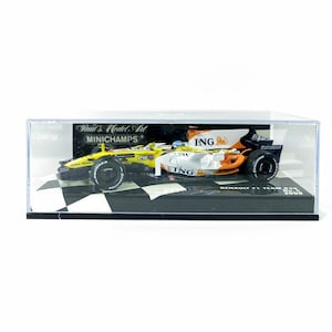 May include: A model Renault F1 race car in a clear display case. The car is yellow, white, and orange with black tyres. The display case sits on a black and white chequered base.