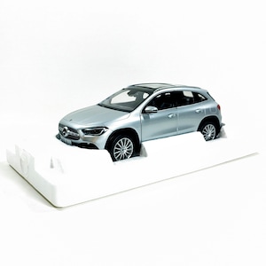 Può includere: Un'auto modello argentata, una Mercedes-Benz GLA, è esposta su una piattaforma bianca. Il SUV in miniatura ha un tetto nero, ruote dettagliate e una finitura lucida. L'auto è su uno sfondo bianco.