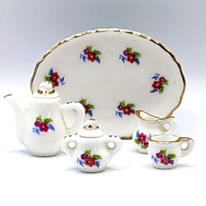 Könnte beinhalten: Ein Miniatur-Porzellan-Teeservice mit Teekanne, Zuckerdose, Sahnekännchen, Tasse und Servierplatte. Das Set ist weiß mit goldenen Verzierungen und mit roten und blauen Blumenmustern verziert. Ideal für ein Puppenhaus.