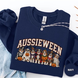 Peut inclure: Un sweat-shirt bleu marine à col rond avec une impression graphique de sept chiens bergers australiens portant divers costumes d'Halloween, dont un squelette, un fantôme, une sorcière, un vampire, une citrouille, un cow-boy et une momie.