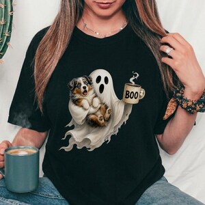 Peut inclure: Un t-shirt noir avec un motif représentant un fantôme blanc tenant un chiot berger australien marron et blanc ainsi qu'une tasse beige avec l'inscription BOO. Le fantôme a une expression surprise avec la bouche ouverte et les yeux écarquillés.