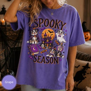 Peut inclure: Un t-shirt à manches courtes de couleur raisin avec une impression graphique portant le texte SPOOKY SEASON. Le motif comprend deux chiens bergers australiens, l'un portant un chapeau de sorcière et une cape, l'autre un costume de fantôme, un manoir hanté et un grimoire.