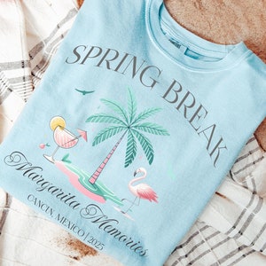 May include: A light blue sweatshirt with the text "Spring Break Margarita Memories Cancun, Mexico 2025" and a pink flamingo illustration.