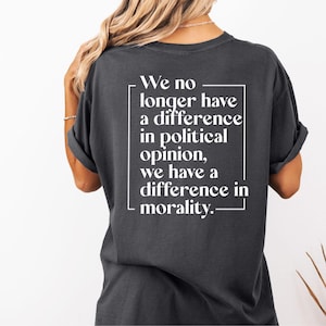 May include: Dark gray t-shirt with white text. The text, enclosed in a white rectangle, reads: "We no longer have a difference in political opinion, we have a difference in morality."