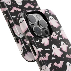 May include: Black phone case with a repeating pattern of pink ghosts and bats. The case has a glossy finish and a black camera lens protector. The design is a cute and spooky Halloween theme.