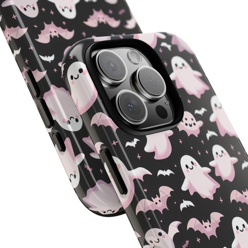 May include: Black phone case with a repeating pattern of pink ghosts and bats. The case has a glossy finish and a black camera lens protector. The design is a cute and spooky Halloween theme.