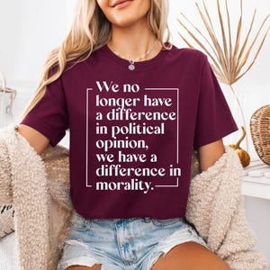 May include: A maroon short-sleeved t-shirt featuring white text enclosed in a rectangular frame. The text reads: We no longer have a difference in political opinion, we have a difference in morality. The shirt has a crew neckline and a standard fit.