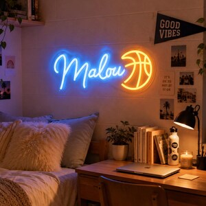 May include: A wall-mounted neon sign featuring the name Malou in glowing blue cursive script next to a bright yellow basketball graphic. The sign emits a vibrant light against a white wall, creating a focal point in a bedroom setting.