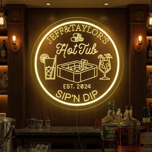 May include: A glowing neon sign with the text "JEFF & TAYLOR'S Hot Tub" and "SIP'N DIP". The sign features a hot tub graphic, cocktail glasses, and the year "EST. 2024". The sign is mounted on a wooden wall.