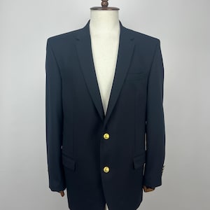 May include: A black blazer with gold-colored buttons and a notched lapel. The blazer is displayed on a wooden mannequin. The jacket has two front pockets and a breast pocket. The sleeves have gold buttons.